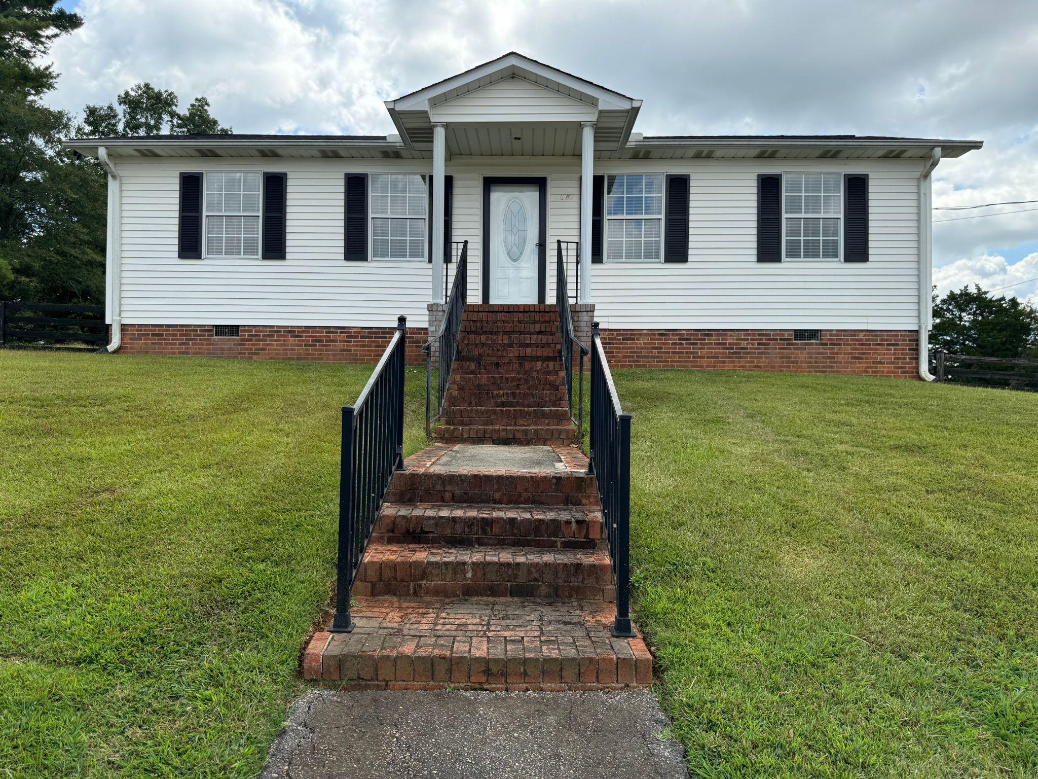 A front view of the East Coast Granite & Tile showroom building, showing a single-story, white-paneled structure with brick foundation . The building is centered on a grassy lawn positioned behind a variety  natural stone slabs for countertops.