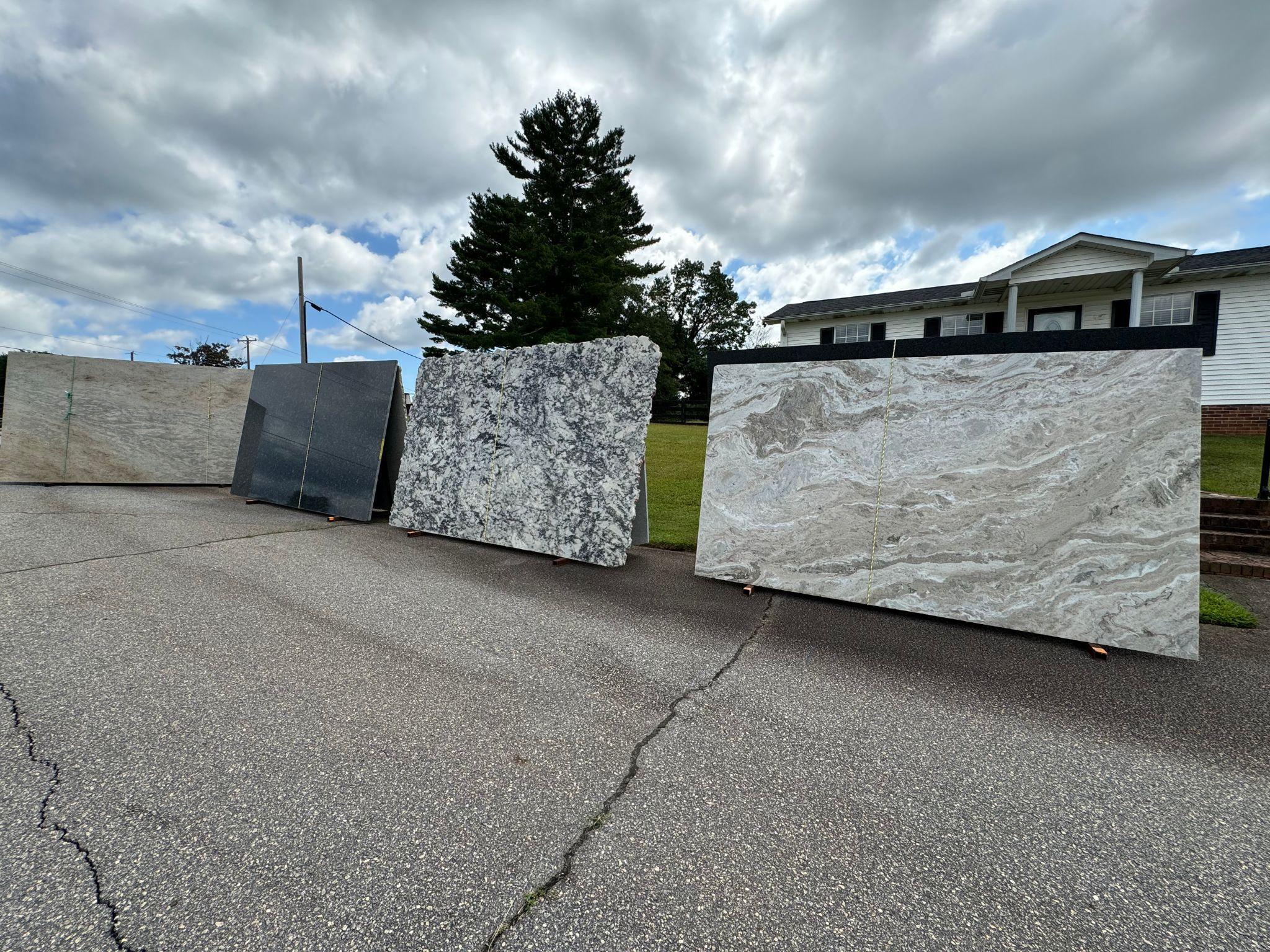 A view from the front steps of the East Coast Granite & Tile - Travelers Rest showroom, looking outward at the street and parking area. Various large granite slabs are displayed outdoors offering a scenic look over the busy road in front of the showroom.